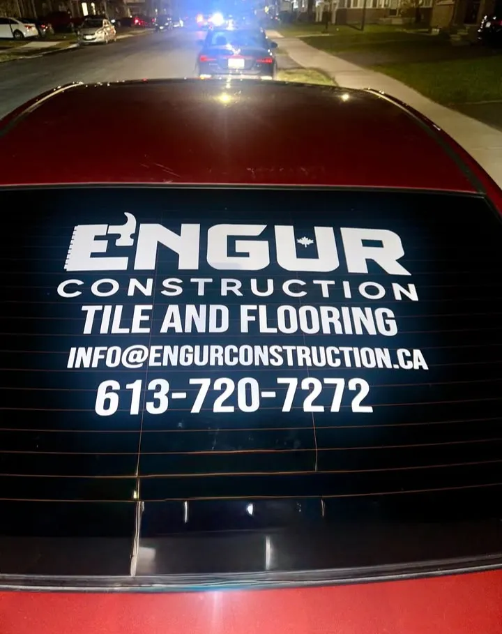 Rear window of a red sedan with Engur Construction lettering, service line and contact details in white vinyl