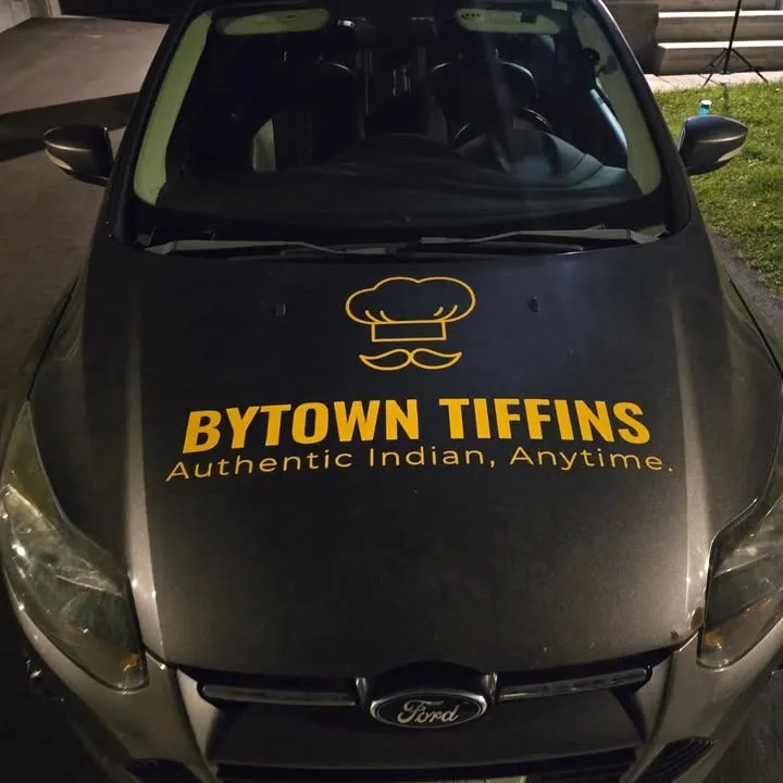 Yellow chef-hat logo and Bytown Tiffins lettering in cut vinyl on the hood of a grey sedan